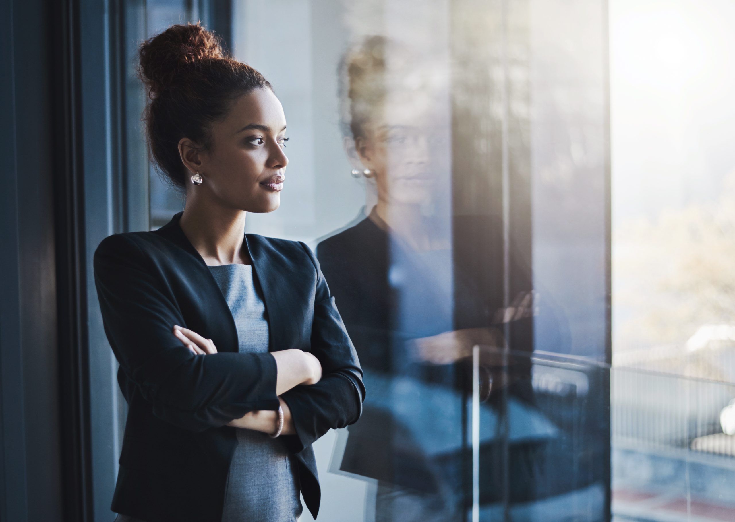 Business woman, window and thinking for vision, goals and future of career with ideas, mission and mindset. Young businesswoman, focus and ambition in workplace with memory, reflection and dream - nothing else in background